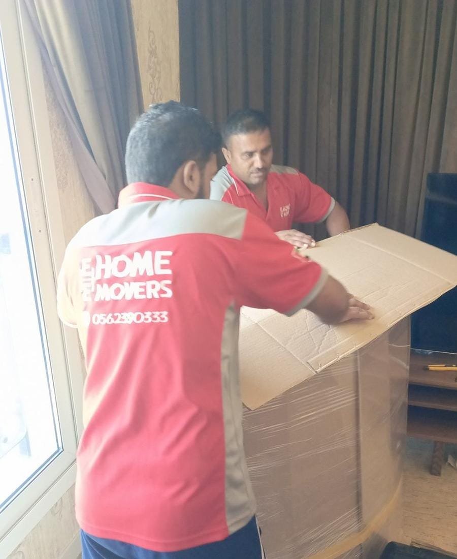 E Home Movers crew in branded red uniforms packing a protected furniture item